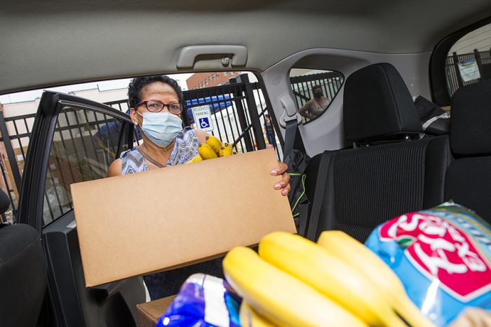woman in mask loads box of food into car