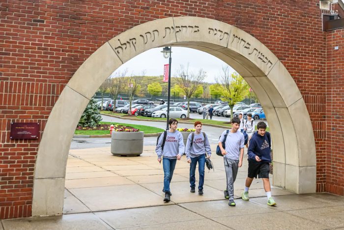 four gann academy student walking under an arch etched with hebrew letters